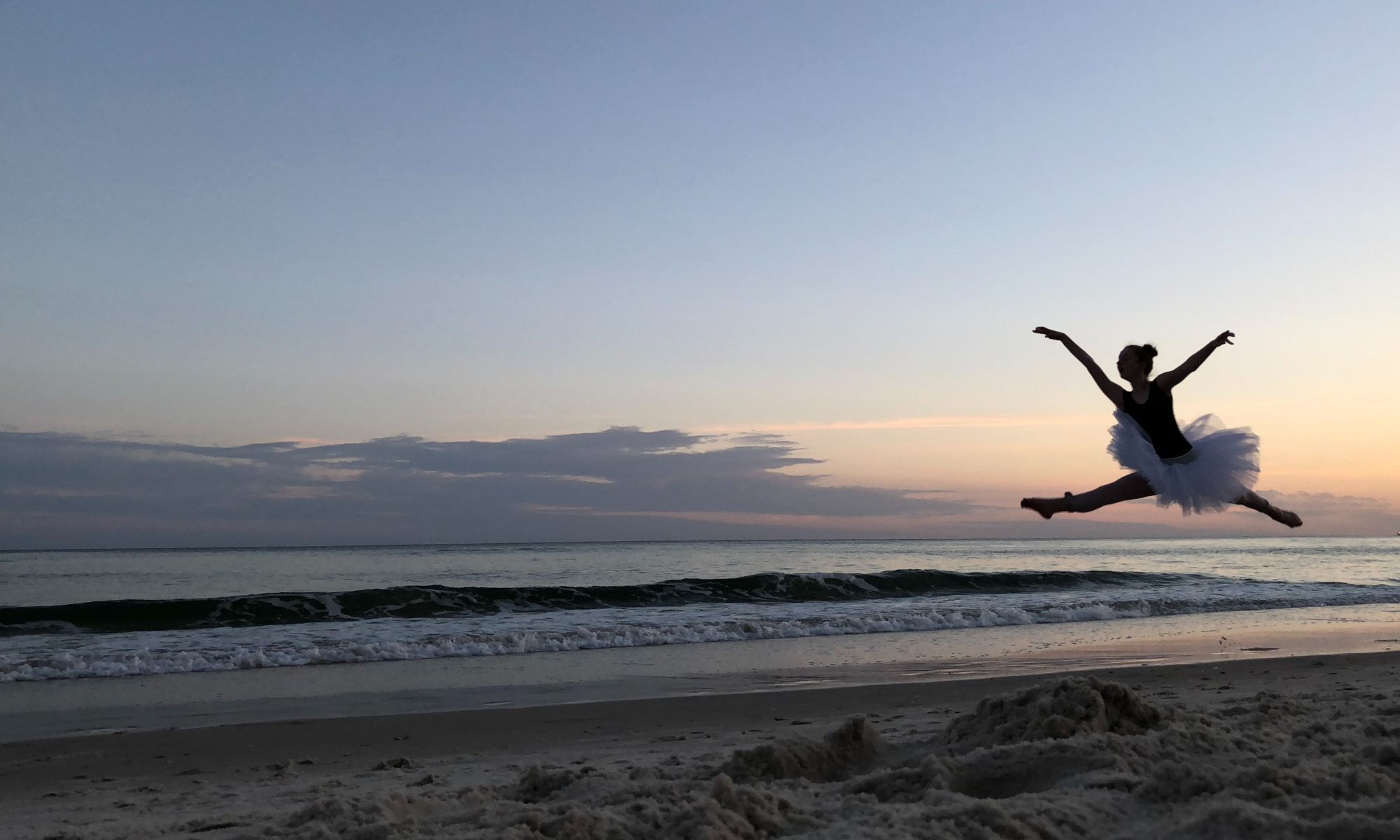 ballerina leaps on beach at sunset