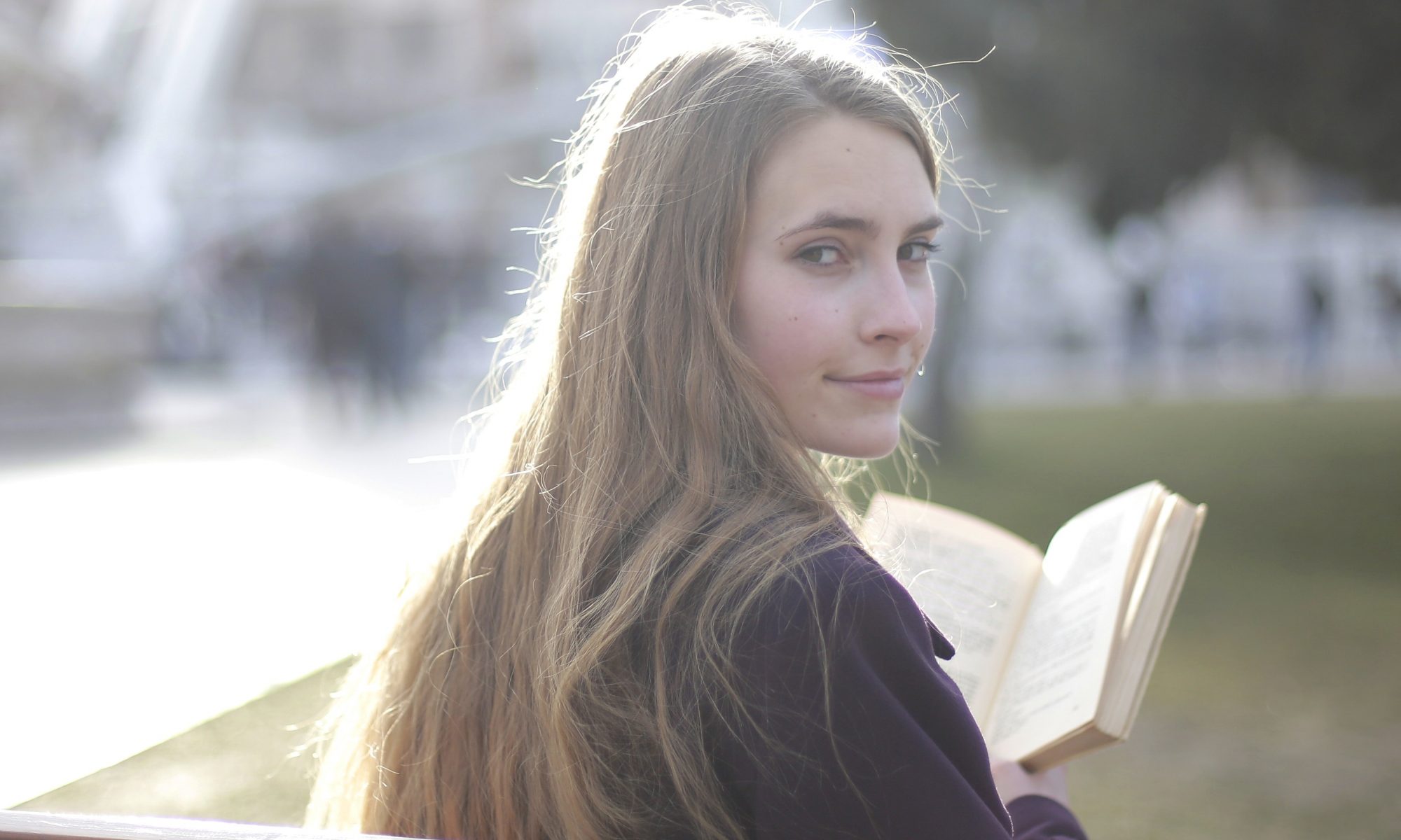girl-with-long-hair-sits-on-bench-holds-book