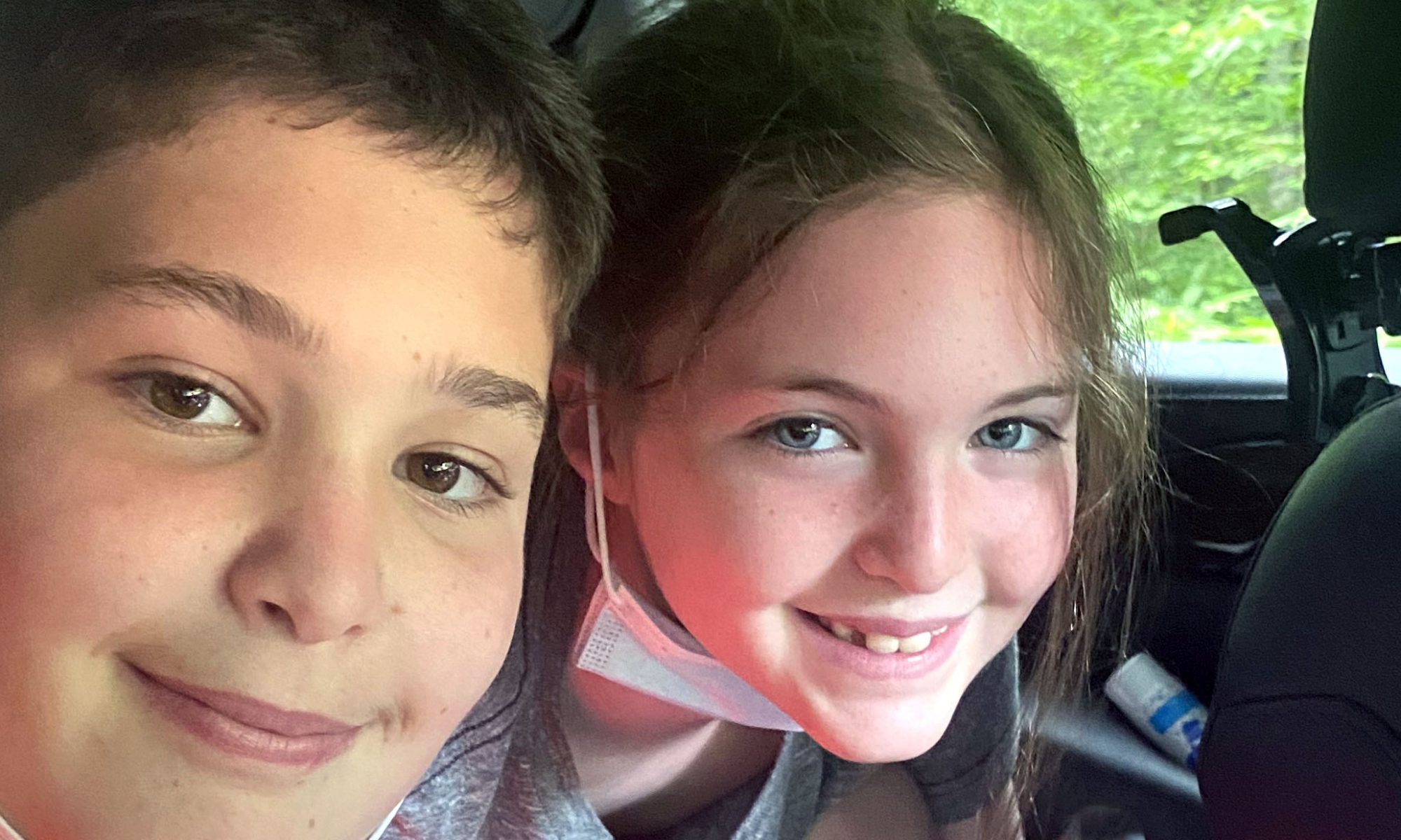 two-children-ride-in-backseat-of-car-smiling