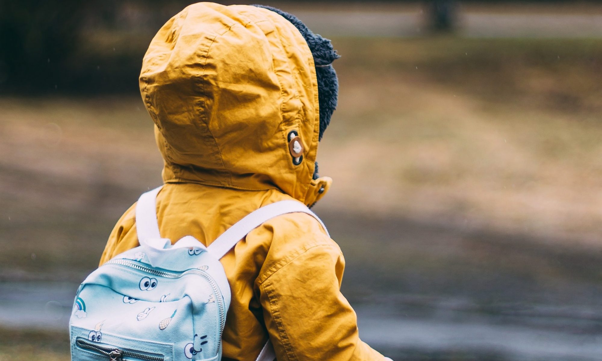 small-child-in-yellow-raincoat-with-blue-backpack-walks-across-grass-photo-by-daiga-ellaby-on-unsplash
