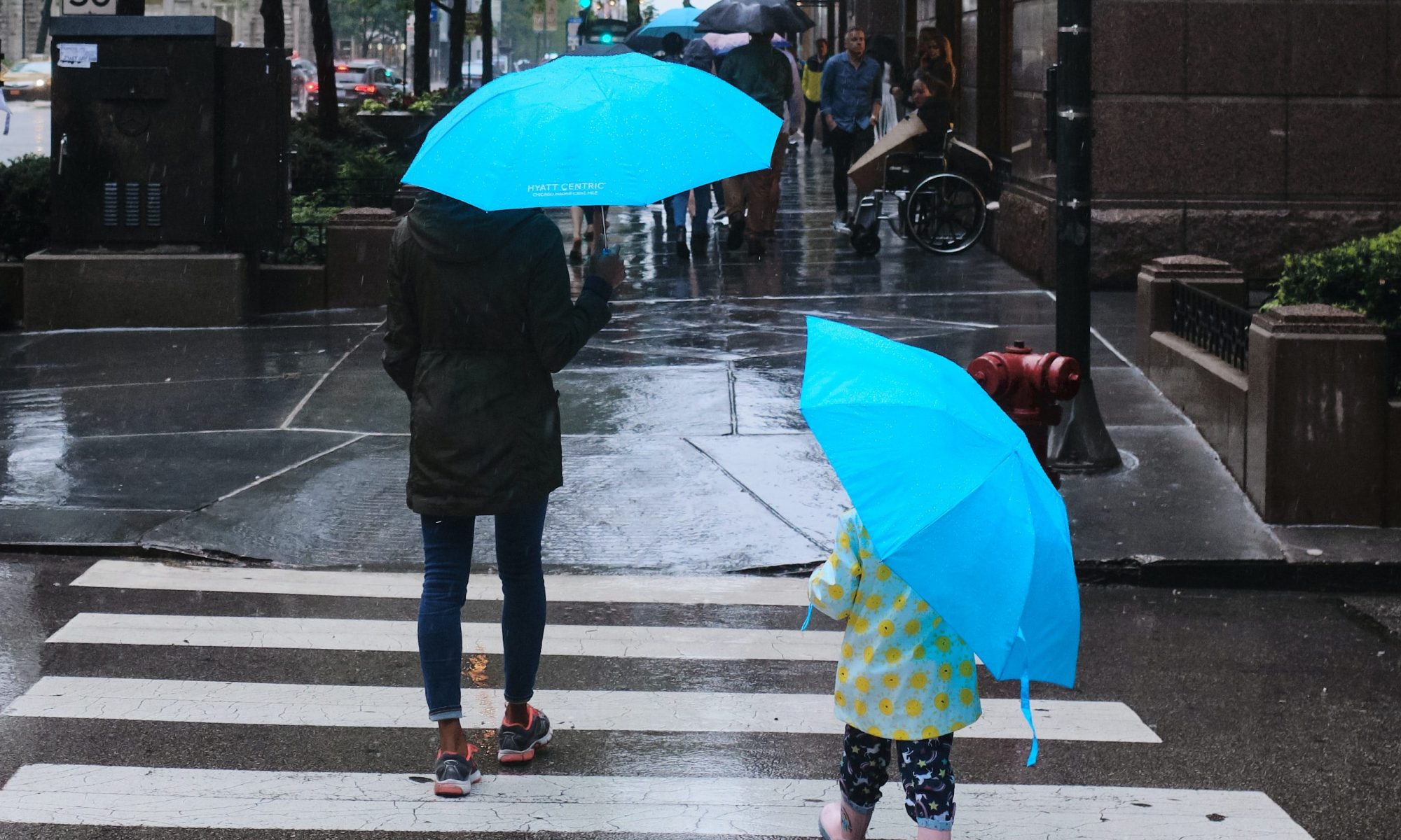two-people-cross-in-crosswalk-carrying-bright-blue-umbrellas-credit-ian-battaglia-on-unsplash
