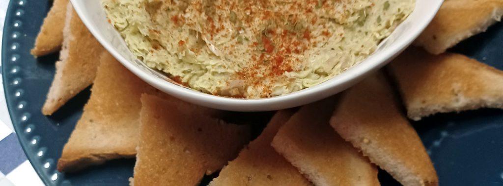 Bowl of homemade artichoke dip garnished with chopped parsley and paprika, and served with gluten free toast triangles. Image by recipe creator, Allergy Dragon (Chef Martha Morgan.)