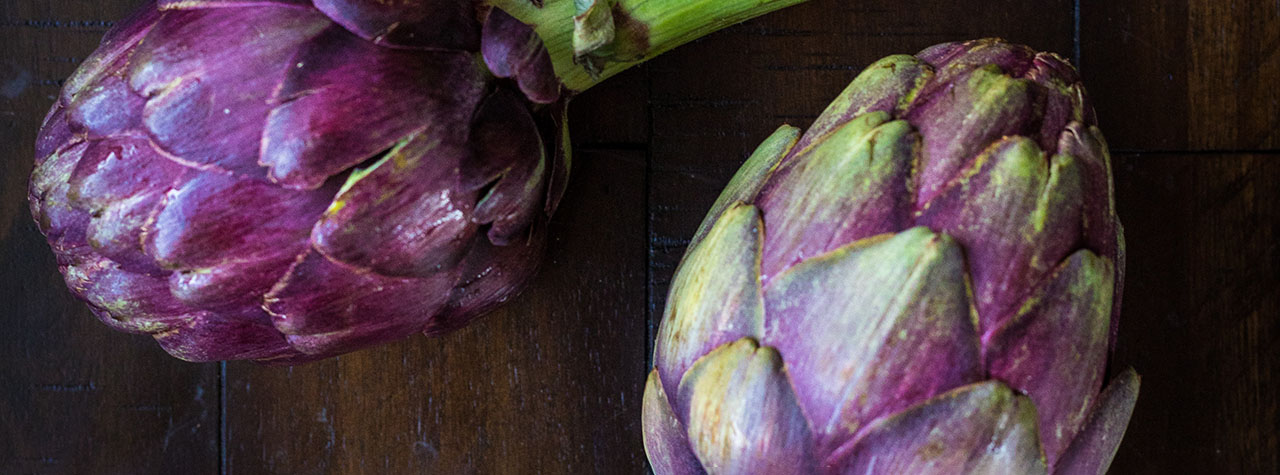 Green and purple artichokes on dark brown wood background. Image by Heather Gill on Unsplash.