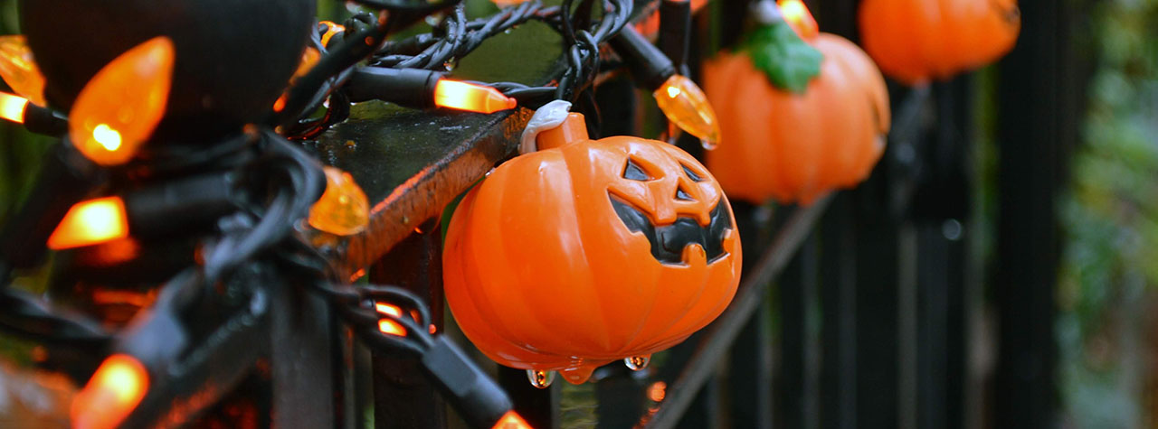 String of small plastic jack-o-lanterns and Halloween fairy lights strung on a black wrought iron fence. Image by John Hayler on Unsplash.