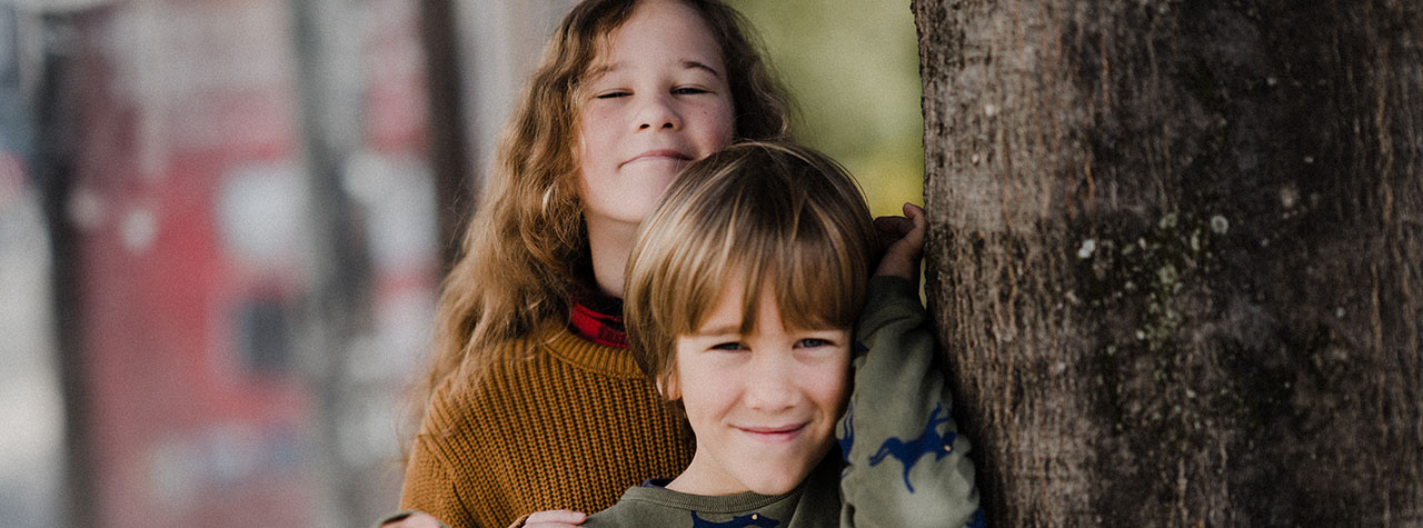 Two young boys stand next to tree and smile for the camera. Image by Annie Spratt on Unsplash.