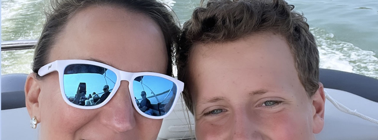 Mom in sunglasses and son sit in the back of a motor boat smiling. Image courtesy of Dr. Julie Sweeney.