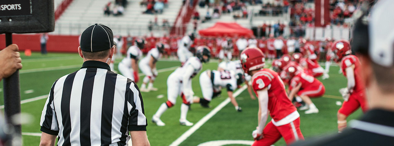 Football referee in black and white striped shirt calls a play in a football game making sure rules are followed. Image by Tim Mossholder on Pexels.