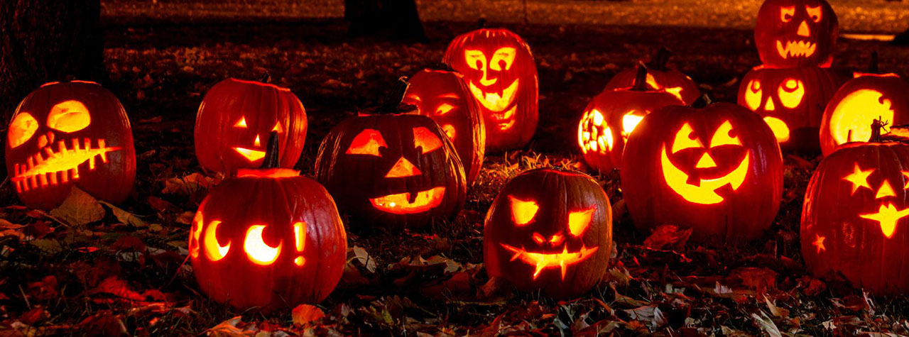 Hand carved pumpkins glow in the dark on fallen leaves. Image by Allergy Force on Canva.