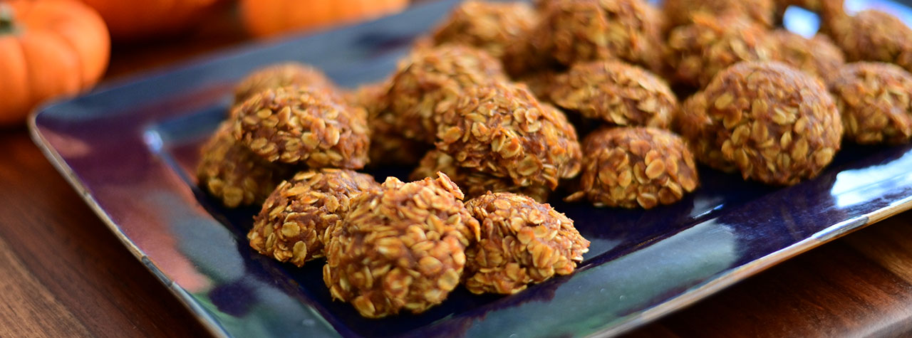 Mouthwatering homemade whole grain pumpkin cookies on a rustic, dark blue platter with bright orange pumpkins in the background. Image by MBR Imaging.