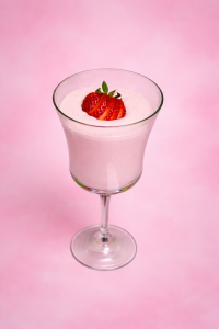 Allergy-friendly Pink Dream Fluff garnished with a sliced strawberry in a crystal wine glass with a pink background. Image by Allergy Dragon.