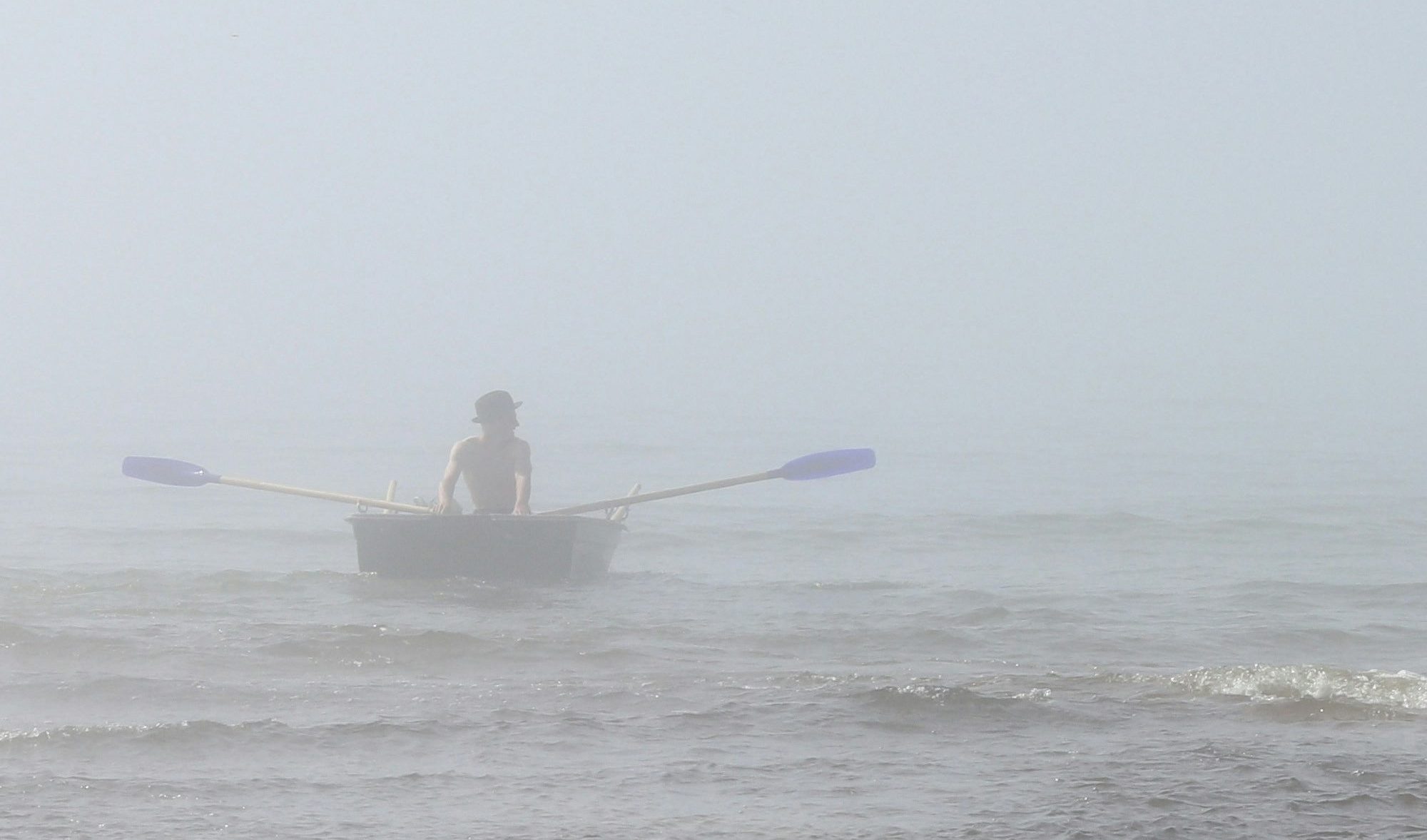 Person rows into a foggy sea in a tiny rowboat. Image by Geda Zyvatkauskaite on Unsplash.
